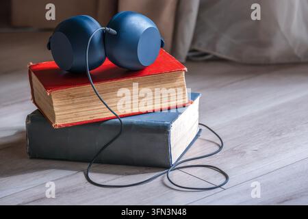 Kopfhörer, die auf gestapelten Vintage-Büchern platziert sind, symbolisieren die Verschmelzung von traditionellem Lesen mit digitalem Audioinhalt und Lernen Stockfoto