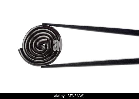 Liquorice-Rad Einzelstück zwischen schwarzen Stäbchen, isoliert auf weißem Hintergrund. Stockfoto