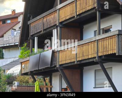 zwei Photovoltaikmodule, die auf einem authentischen Holzbalusterzaun montiert sind, umgeben von erfrischendem Sommergrün und tiefblauem Himmel Stockfoto