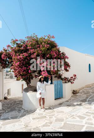 Asiatische Frau wandert durch die malerischen Straßen von Lefkes in Paros, Griechenland, wo leuchtende Bougainvillea-Blüten weiß getünchte Gebäude umrahmen unter Stockfoto