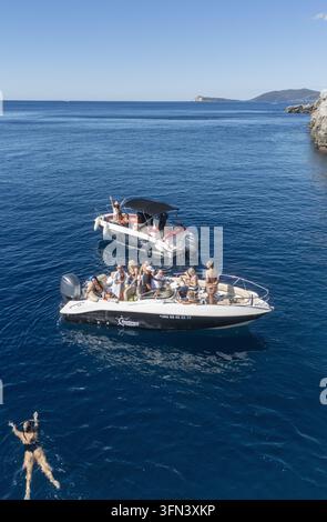 Luftaufnahme von zwei Motorbooten, die mit Menschen gefüllt sind, die einen sonnigen Tag im tiefblauen Meer in der Nähe der felsigen Küste von Tivat, Gemeinde Tivat, Montenegro genießen Stockfoto