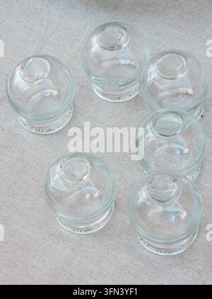 Traditionelle Glasbecher der Kupping-Therapie sind in einer Draufsicht auf neutralem Leinenstoff angeordnet. Diese Anordnung zeigt die Becher, die in einer therapeutischen P Stockfoto