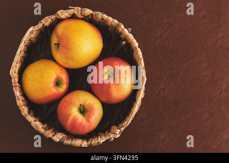 Frische reife gelbe und rote Äpfel in einem Weidenkorb auf braunem Hintergrund Stockfoto