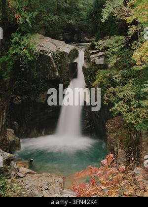 Wasserfall stürzt in ein türkisfarbenes Becken zwischen moosigen Felsen in einem Wald in Nagano, Japan. Stockfoto