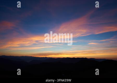 Der faszinierende Sonnenuntergang zeigt den Himmel mit leuchtenden Rosa-, Orange- und Blautönen. Weiche, schimmernde Wolken erstrecken sich über den Horizont, während Silhouetten entfernter Berge dramatische und ruhige Szenen schaffen. Stockfoto