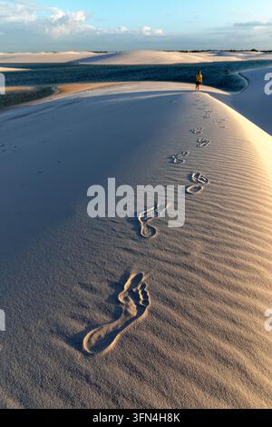 Eine detaillierte Nahaufnahme von Wanderer-Fußspuren in den unberührten weißen Sanddünen von Lencois Maranhenses, mit entfernten Wanderern im Hintergrund. Stockfoto