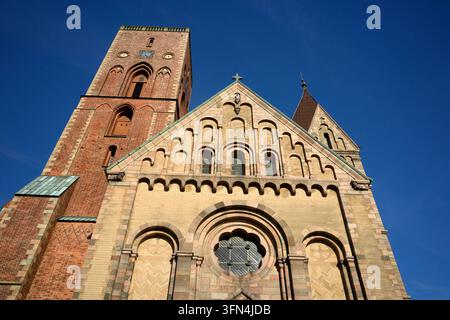Niedriger Blick auf die kunstvolle romanische Fassade der Ribe Kathedrale mit Rundfenster, gewölbten Details und hohem Backsteinturm vor blauem Himmel. Stockfoto