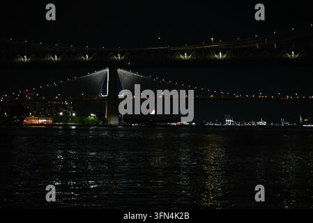 Luftbild der Brooklyn Bridge bei Nacht über dem East River mit Stadtlichtern, die sich auf dem Wasser spiegeln, und einem Halbmond New York, New Stockfoto