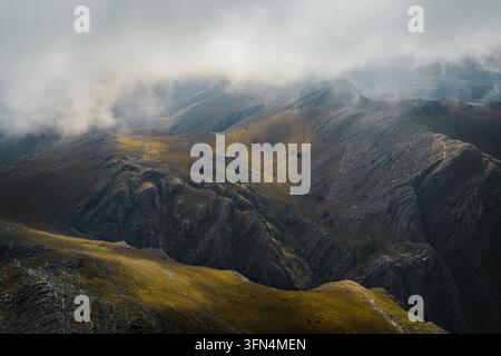 Blick auf schroffe Berghänge mit felsigen Texturen und Flecken aus goldenem Gras, die teilweise von tief hängenden Wolken in der Sierra de La Ventana, Bueno, verdeckt sind Stockfoto