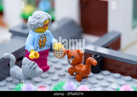 Tambow, Russische Föderation – 24. September 2026 Eine Lego-Oma-Minifigur steht vor einem Haus, hält einen Miniatur-Keks und füttert eine orange C Stockfoto