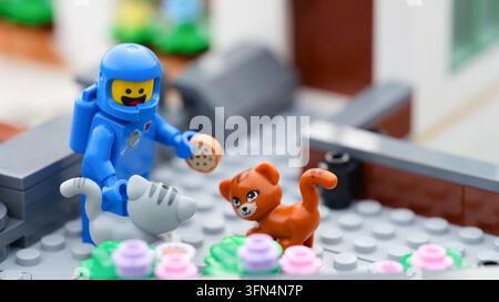 Tambow, Russische Föderation – 24. September 2026 Eine blaue Lego-Astronauten-Minifigur steht vor einem Haus und hält einen Miniatur-Keks in der Hand, umgeben von einem Stockfoto