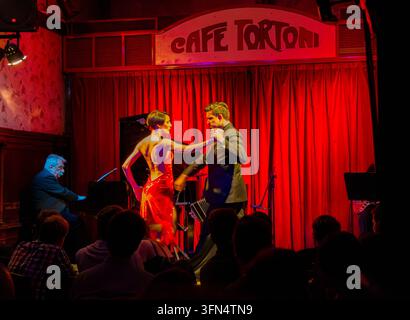 Buenos Aires, Argentinien – 29. Juli 2017: Frau in rückenfreiem rotem Kleid tanzt ausdrucksstarke Tangofigur mit männlichem Partner vor Live-Publikum im Cafe Tor Stockfoto