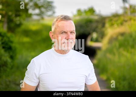 Selbstbewusster reifer Mann steht im Freien mit einem ernsten und konzentrierten Ausdruck in natürlicher grüner Umgebung. Authentisches Lifestyle-Porträt, das darstellt Stockfoto