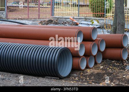 Eine Nahaufnahme von gestapelten braunen und schwarzen Wellplatten-Drainageleitungen, die auf erdigem Boden neben einem Zaun an einer städtischen kommunalen Baustelle ruhen Stockfoto