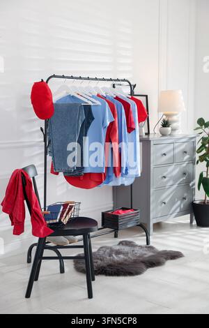 Verschiedene Kleidungsstücke hängen an einem Kleiderständer, Baseballkappe und Dekoration im Innenraum Stockfoto