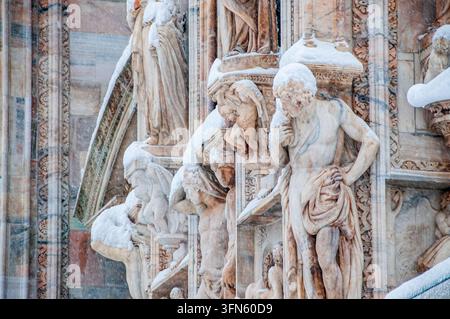 Eine detaillierte Nahaufnahme, die die Marmorskulpturen und Bas-reliefs an der Fassade des Mailänder Doms zeigt. Die geschnitzten menschlichen Figuren sammeln sich in weichem Weiß Stockfoto