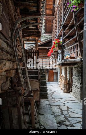 Eine bezaubernde und schmale steingepflasterte Gasse zwischen den historischen Walser-Häusern von Pedemonte. Die Nahaufnahme zeigt Blockwände, Balkone, die mit Stockfoto