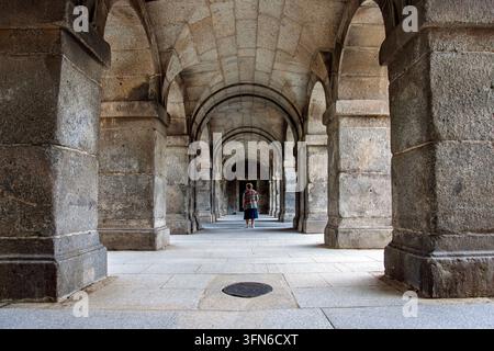 Eine Frau geht durch eine majestätische Renaissance-Loggia im San Lorenzo de El Escorial, einer historischen königlichen Stätte in Madrid, Spanien. Grandiose Steinarchitektur. Stockfoto