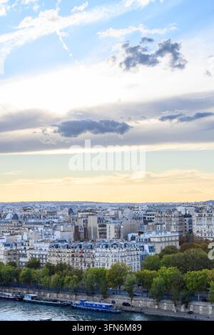 Pariser Skyline in sanftem Dämmerungslicht getaucht. Die Seine fließt sanft unter baumbewachsenen Ufern. Die Stadtlandschaft erstreckt sich mit Dächern und fernen Türmen. Der Himmel hält Stockfoto