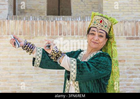 Eine usbekische Dame in traditioneller Kleidung spielt Qairaqs (flache ovale Steine) ähnlich wie Kastagnetten vor der Mir-i-Arab-Madrasa in Buxara, Usbekistan Stockfoto