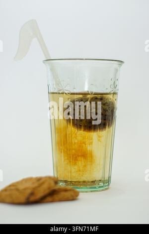 Teesieb in Form einer Musiknote, das in einem Glas Tee zieht, mit Keksen auf weißem Hintergrund Stockfoto