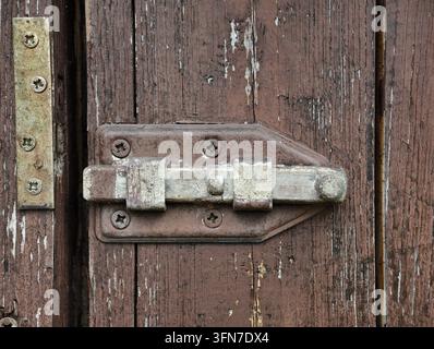 Nahaufnahme einer verwitterten Holztür, die mit altem Metallschloss, Scharnier, Schrauben und abblätternder Farbe gesichert ist. Rustikale Oberflächentextur, abgenutzte Handwerkskunst und Stockfoto