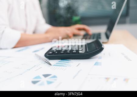 Rechner auf Finanzberichten neben einem Laptop in einem modernen Büro, während ein Profi arbeitet, repräsentierend Buchhaltung, Budgetierung, Finanzen, Datenanalyse Stockfoto