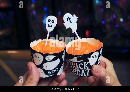 Nahaufnahme eines Paares, das mit orangefarbenen Halloween-Trifle-Cupcakes auf einer Party anstößt Stockfoto