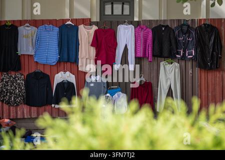 Gebrauchte Kleidung, die an Kleiderbügeln an einem rostigen Wellblechzaun an einem informellen Straßenmarkt in Bălți, Moldau, hängt, mit verschiedenen Jacken Stockfoto