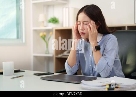 Asiatische Geschäftsfrau leidet unter Kopfschmerzen und Bürosyndrom am Schreibtisch Stockfoto