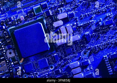 Makroansicht eines blau getönten Mikrochips, der auf einer komplexen Leiterplatte mit elektronischen Komponenten und Anschlüssen montiert ist. High-Tech-Hintergrundkonzept für Co Stockfoto