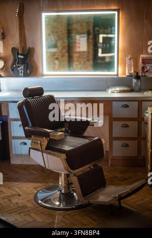Gemütliches Interieur eines Friseursalons mit klassischen Vintage-Stühlen, beleuchteten Spiegeln und professionellen Werkzeugen. Stockfoto