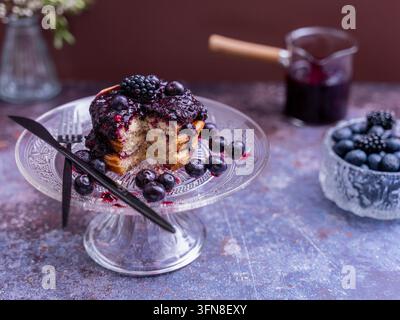 Nahaufnahme von fluffigen Pfannkuchen mit Beerenkompott und frischen Beeren, serviert auf einem eleganten Glas-Kuchenständer Stockfoto