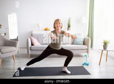 Fröhliche Seniorin macht Lunges beim häuslichen Training im Wohnzimmer, Kopierraum. Sportliche reife Frau führt einen gesunden Lebensstil, bleibt fit oder verliert Gewicht Stockfoto