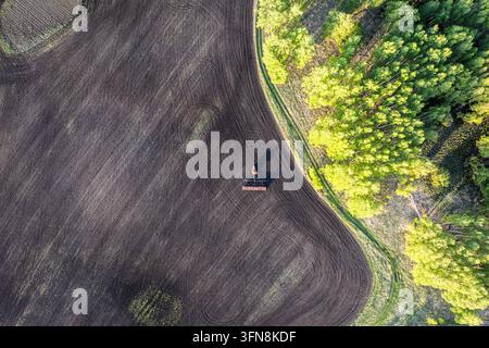Blick auf ein Feld in der Nähe eines Waldes aus einer Drohne, Blick von oben auf eine Agrarlandschaft, ein lockiges Feld und ein kleiner Traktor. Stockfoto