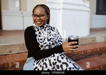 Fröhliche junge Frau mit Brille sitzt auf Stufen draußen Stockfoto