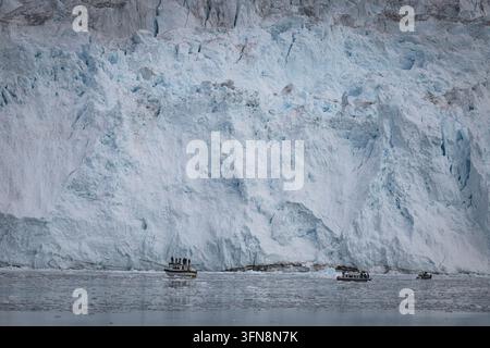 Touristen auf Booten betrachten eine massive arktische Gletscherwand Stockfoto