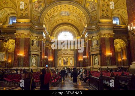 Grandioser Innenblick auf das Heiligtum und das Langhaus der St. Stephans-Basilika in Budapest, Ungarn, mit Touristen, goldenen Bögen und Marmorsäulen Stockfoto