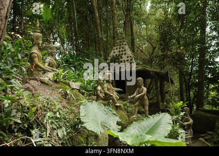 Alte Steinstatuen, die in einem üppigen thailändischen Dschungelgarten verborgen sind Stockfoto