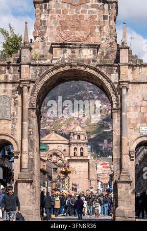 Historischer Steinbogen rahmen eine farbenfrohe Straßenprozession in Cusco, Peru, mit Menschenmassen, die sich auf dem Platz für ein traditionelles Fest inmitten der Kolonialarchitektur versammeln Stockfoto