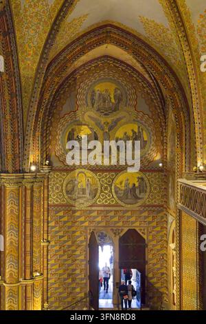 Das kunstvolle Innere der Matthäus-Kirche in Budapest, Ungarn, mit goldenen neogotischen Wandgemälden, gewölbten Decken und einem offenen Eingangsportal. Stockfoto