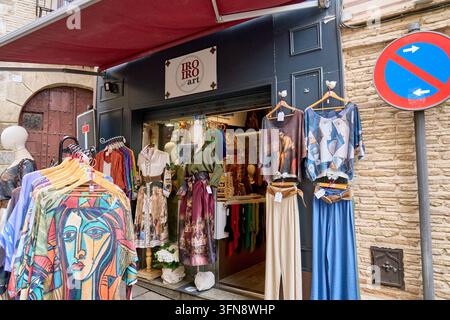 Iro Iro Art Boutique mit bunten bedruckten Oberteilen und Hosen an Kleiderbügeln draußen unter einem roten Markisendach, neben einem Parkverbotsschild, Toledo, Spanien Stockfoto
