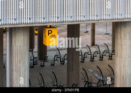 Espoo, Finnland - 1. Oktober 2026: Ein gelbes Fahrradparkzeichen, das unter einer Betonbrücke und einem Bauwerk mit schwarzen Fahrradständern hängt, die installiert sind auf Stockfoto