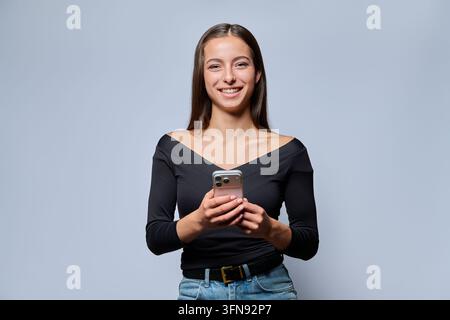 Lächelnde junge Frau hält Smartphone und schaut in die Kamera im Studio Stockfoto