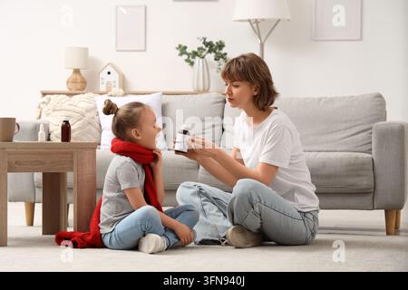 Pädiatrische Gesundheitsversorgung und Kinderwohlbefinden, Mutter gibt ihrer kranken Tochter Flüssigkeit zur Behandlung von Erkältungs- und Grippesymptomen zu Hause in einem gemütlichen Wohnzimmer Stockfoto