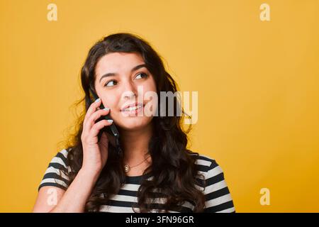 Junge Frau telefoniert mit freundlichem Lächeln vor hellem gelbem Hintergrund Stockfoto