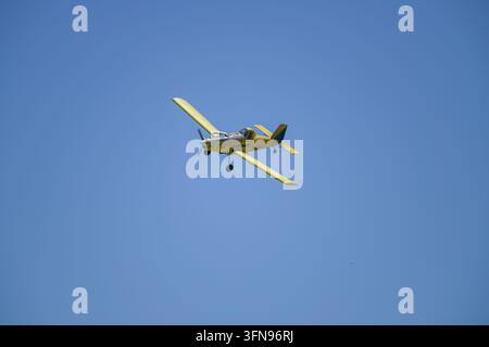 Luftbild eines gelben Sprühflugzeugs, das durch einen klaren blauen Himmel über der Agrarlandschaft von Palouse, Washington, Vereinigte Staaten, fliegt Stockfoto