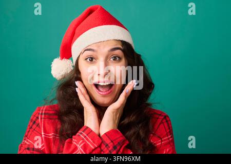 Überraschte junge Frau mit Weihnachtsmannmütze, die den Weihnachtsfeiertag mit fröhlichem Ausdruck feiert Stockfoto