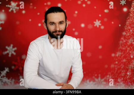 Freundlicher bärtiger Mann, der auf Weihnachts-hintergrund sitzt Stockfoto