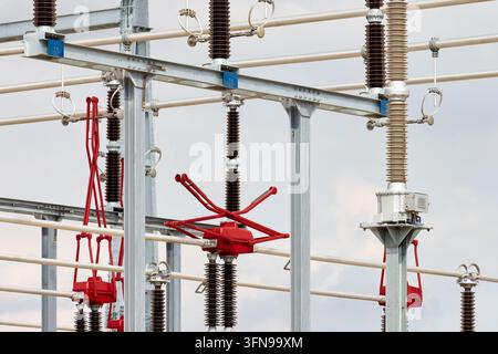 Nahaufnahme einer Hochspannungsunterstation mit Stromschienen, Keramikisolatoren, Stahlträgerbalken und roten mechanischen Pantographenschaltern. Stockfoto